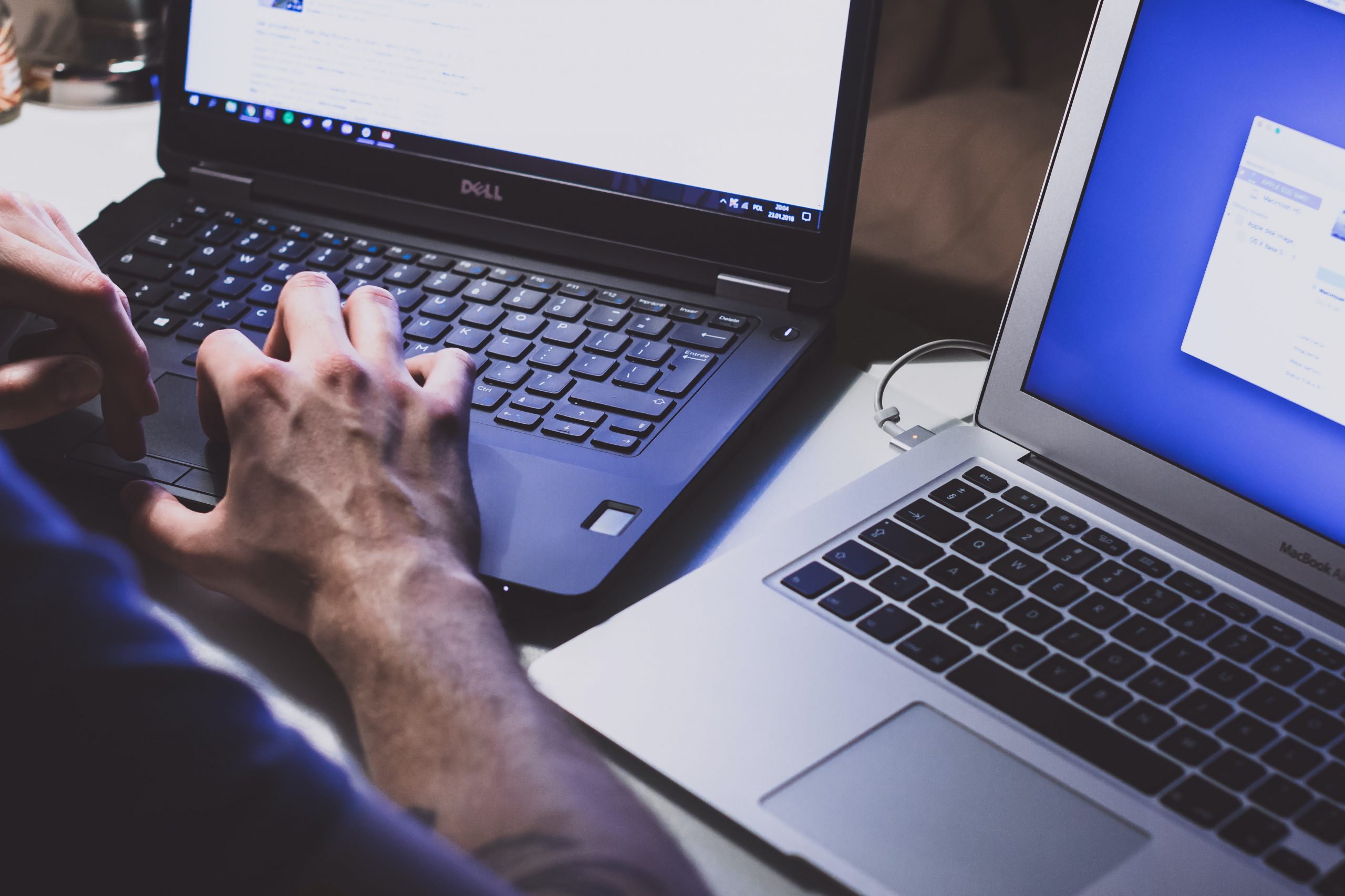 Man working on two laptops at once with his hands on a keyboard