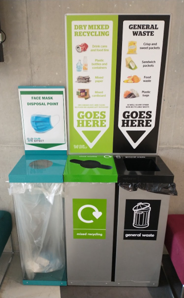 Image of bins on campus green for mixed recycling, black for waste, blue for face covering recycling