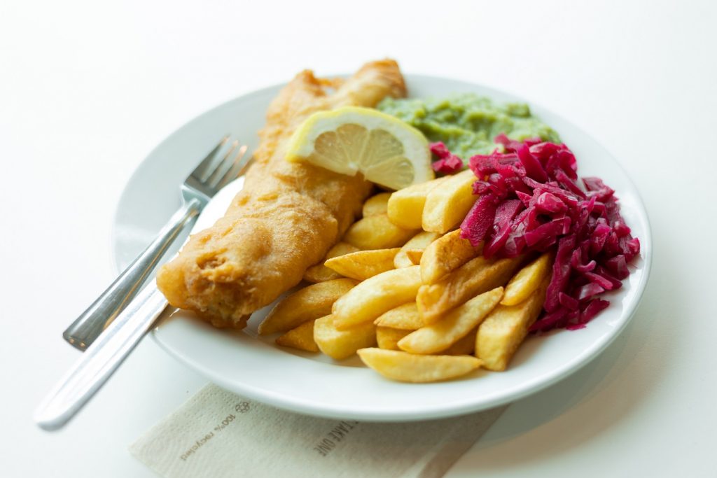 Crispy fish and chips with mushy peas on a white plate,