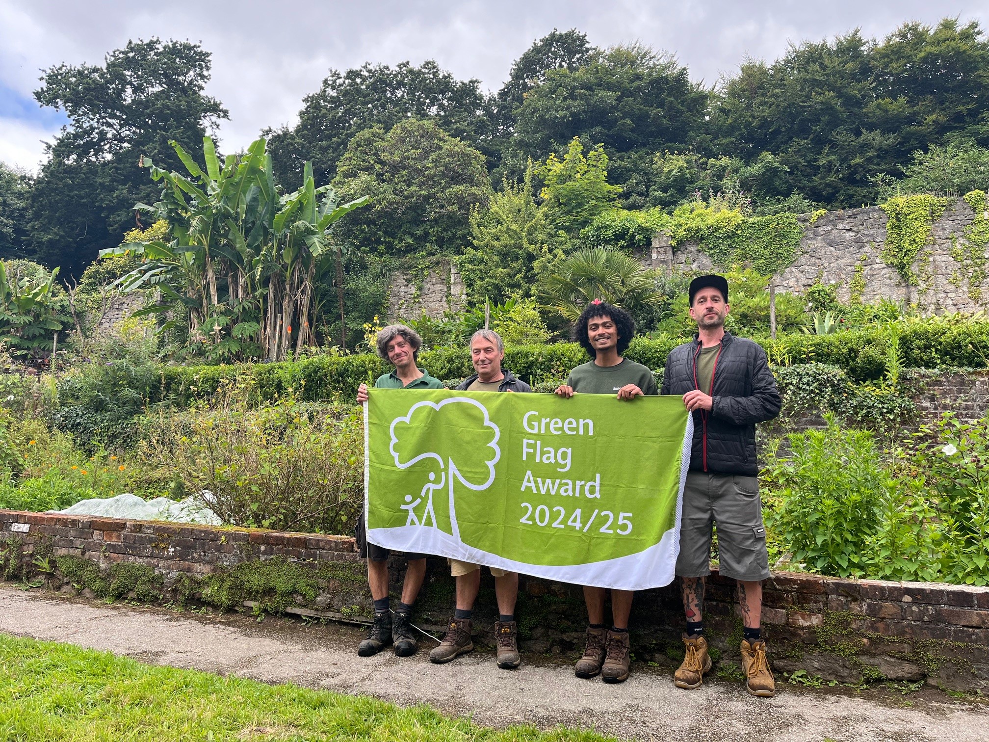 Falmouth Exeter Plus Gardeners holding the Green Flag 2024/24 in the Walled Gardens at Penryn campus.