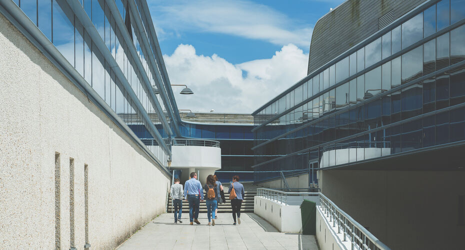 Students walking outside the Daphne Du Maurier building at the Penryn University campus, showing the outside of the building and roofs.