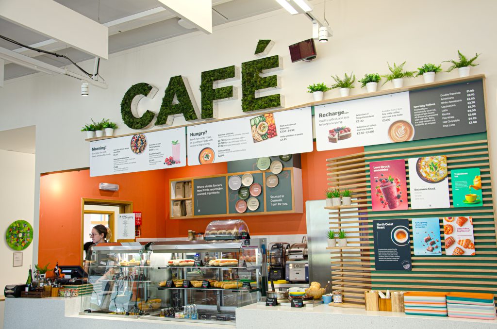 Image of the ESI Cafe at Penryn campus. It shows an array of signage and food available, such as baguettes in glass cabinets and pastries presented on the counter.