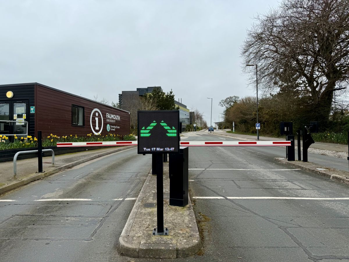 Penryn campus entrance as you drive through the closed barriers with the wooden information hut and daffodils in the background