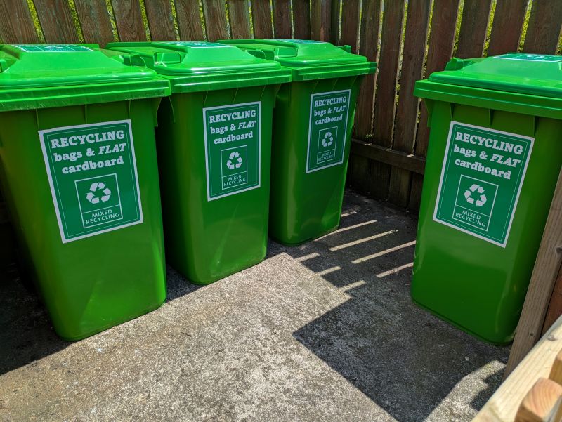 Image of four green waste bins in the bin store with signage saying mixed recycling.