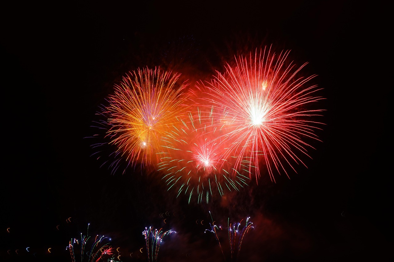a display of three red and orange sparkly fireworks bursting in the black night sky
